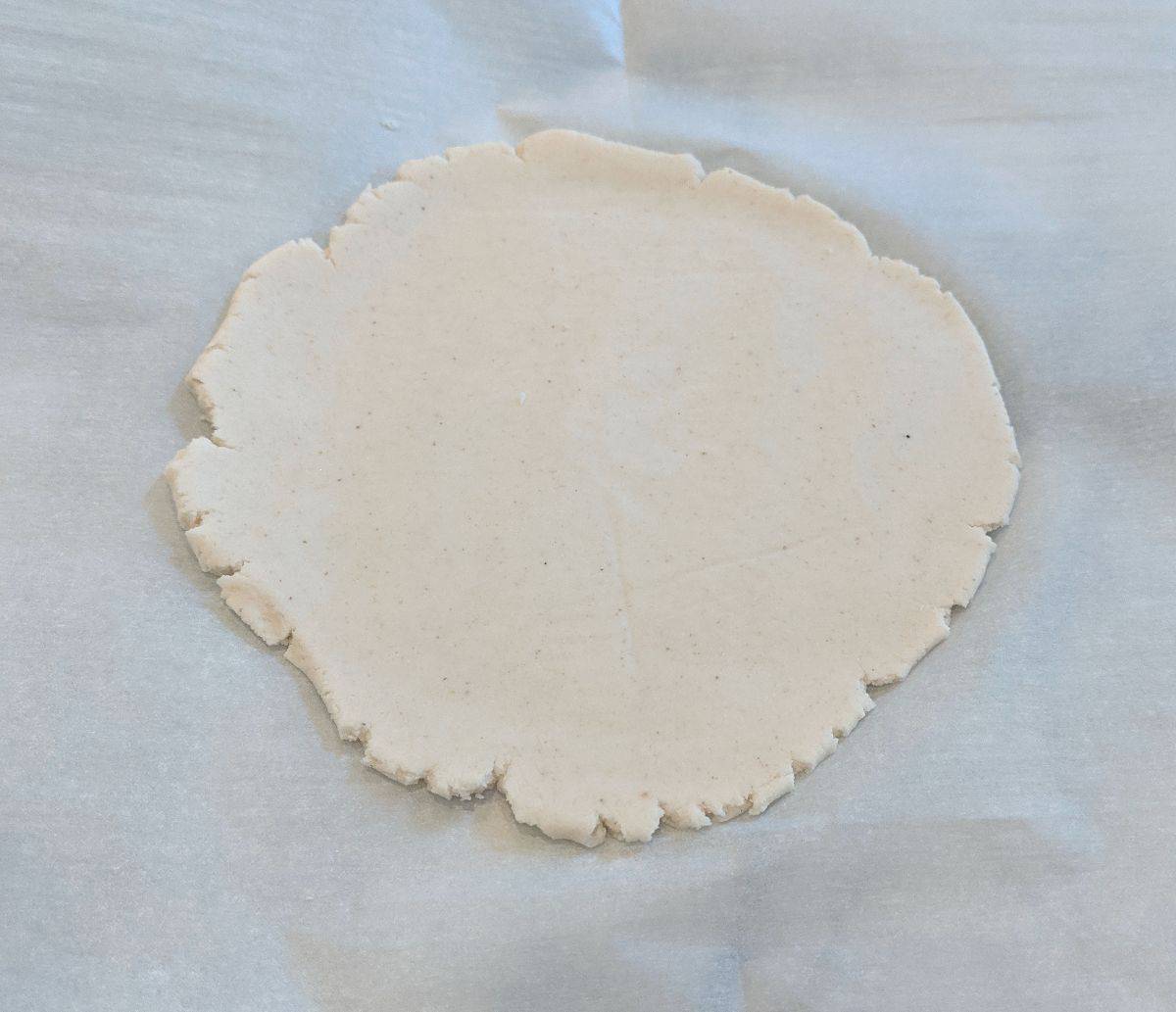 uncooked paleo tortilla on parchment paper with edges slightly cracked