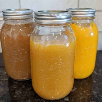 Chicken bone broth in 3 mason jars on a black counter top.