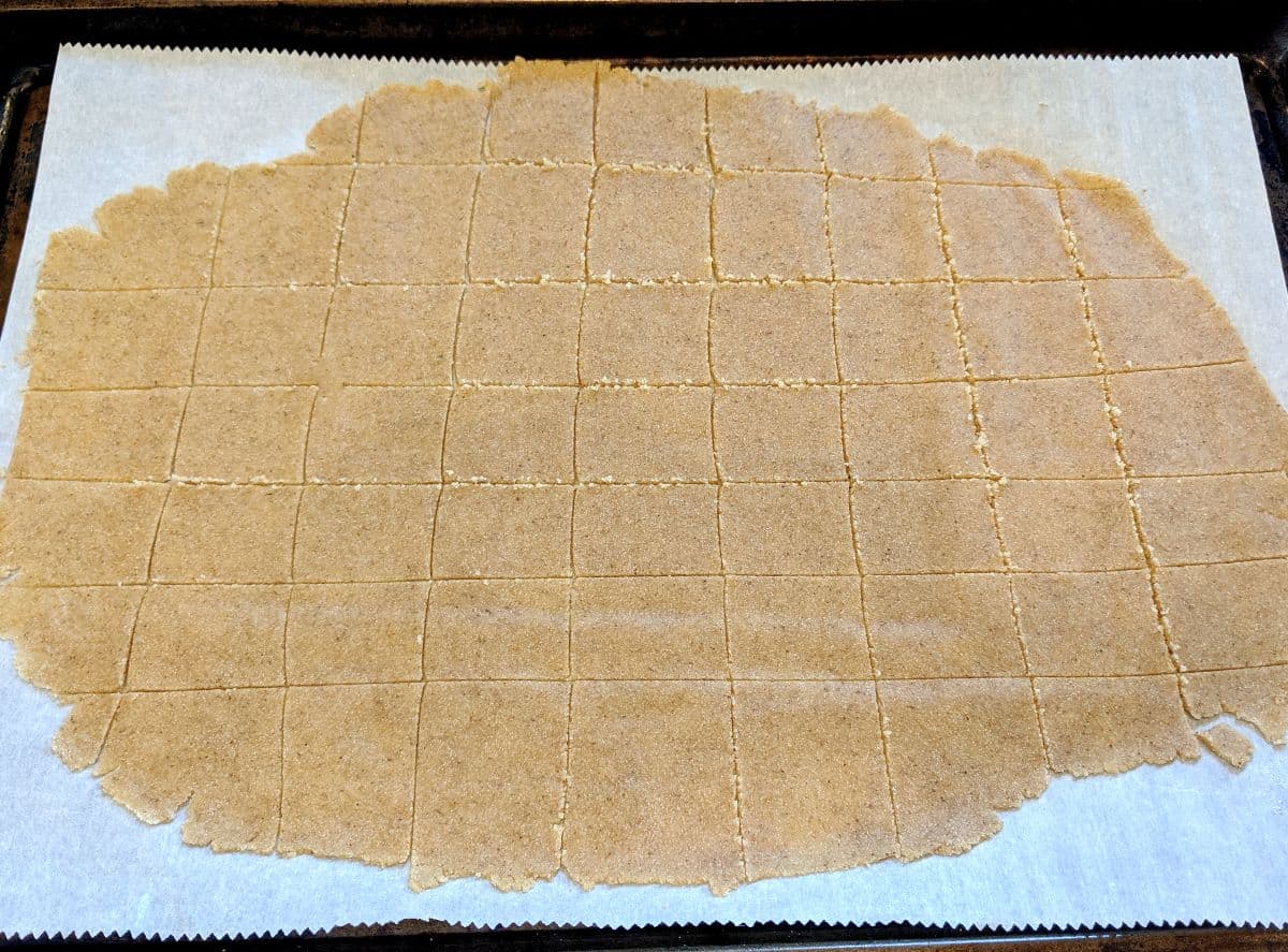 Raw cracker dough on a baking sheet with vertical and horizontal cracker cuts.