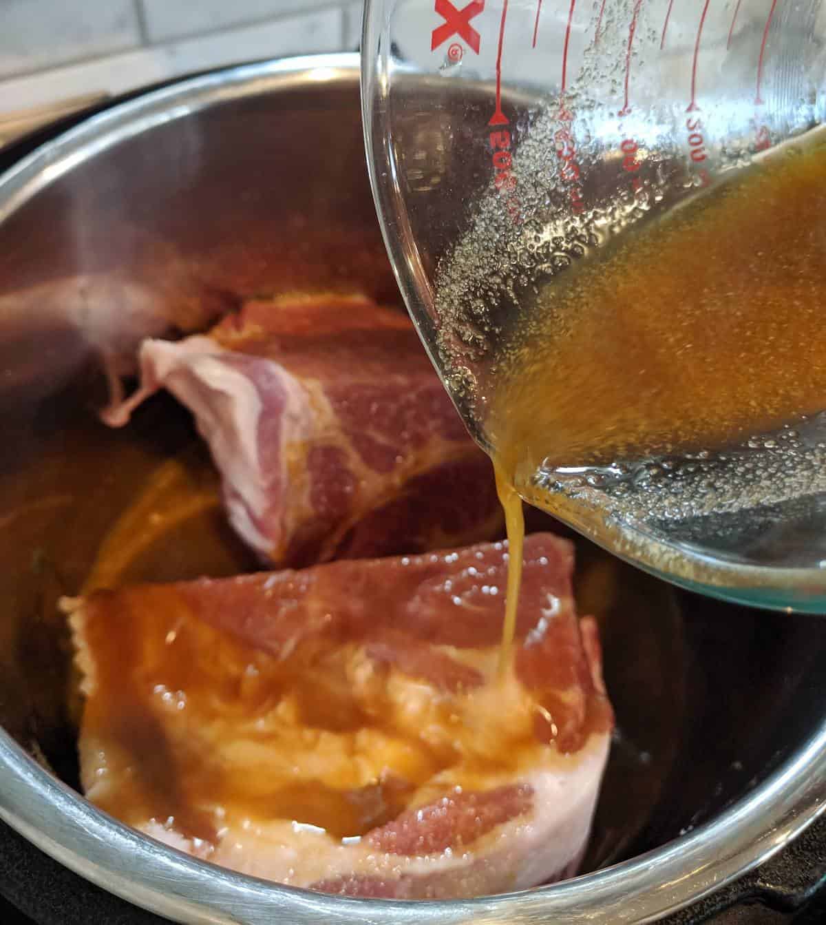Pork butt in the instant pot with sauce being poured over the top.