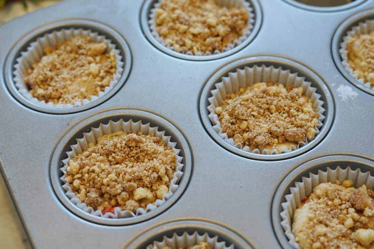 unbaked strawberry rhubarb muffins in a baking tin with a crumb topping added.