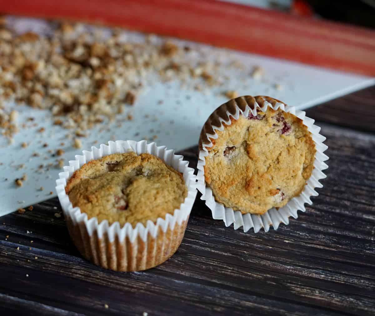 2 strawberry rhubarm muffins on a table with rhubarb in the background.