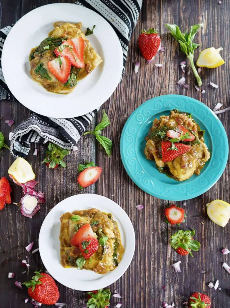 3 plates of strawberry basil chicken on a wooden table with strawberry tops, lemon peels, and basil laying around them