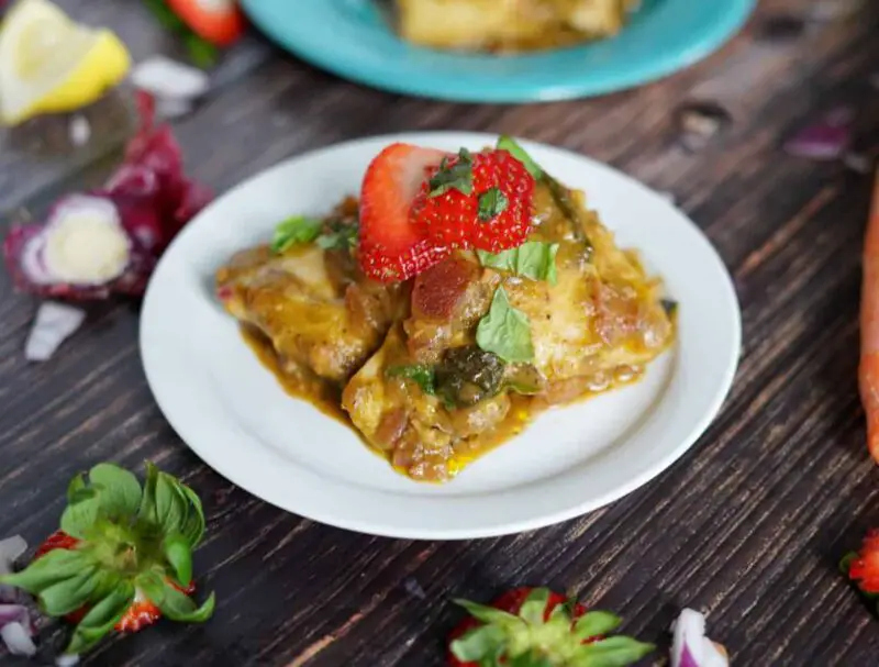 strawberry basil chicken on a small white plate on a wooden table with straberry tops and lemon peels laying nearby