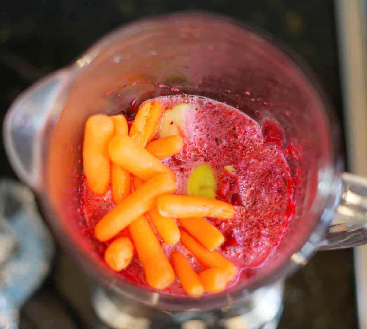 babyc carrots in a blender with a bright pink smoothie base.