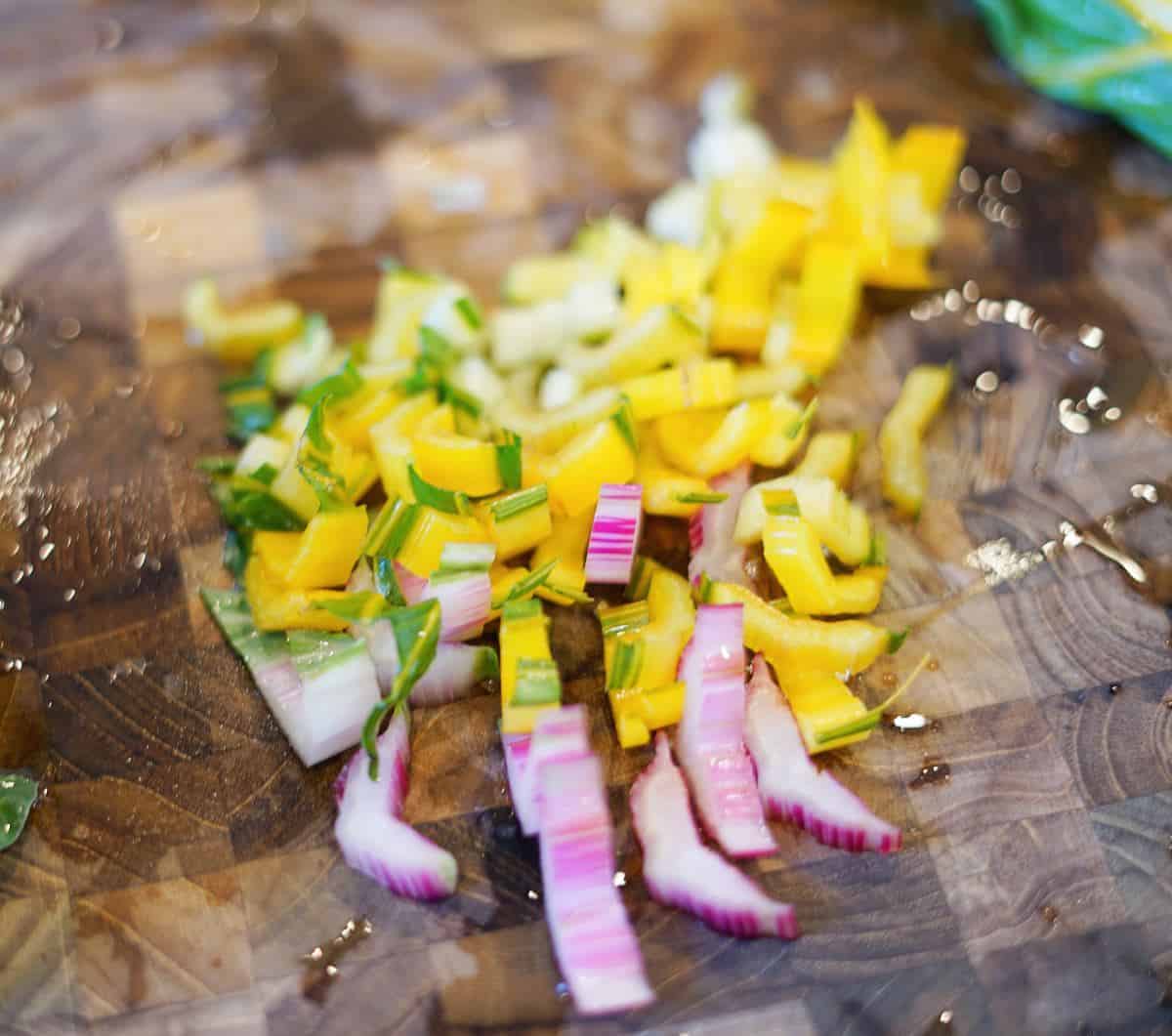 Yellow and pink diced rainbow chard stems on a wooden cutting board.