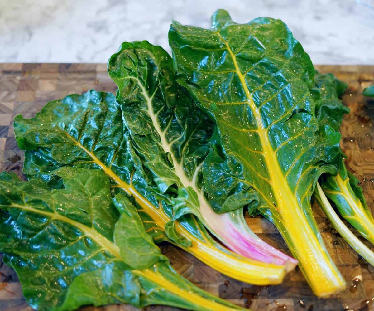 Several brightly colored rainbow chard leaves on a wooden cutting board.