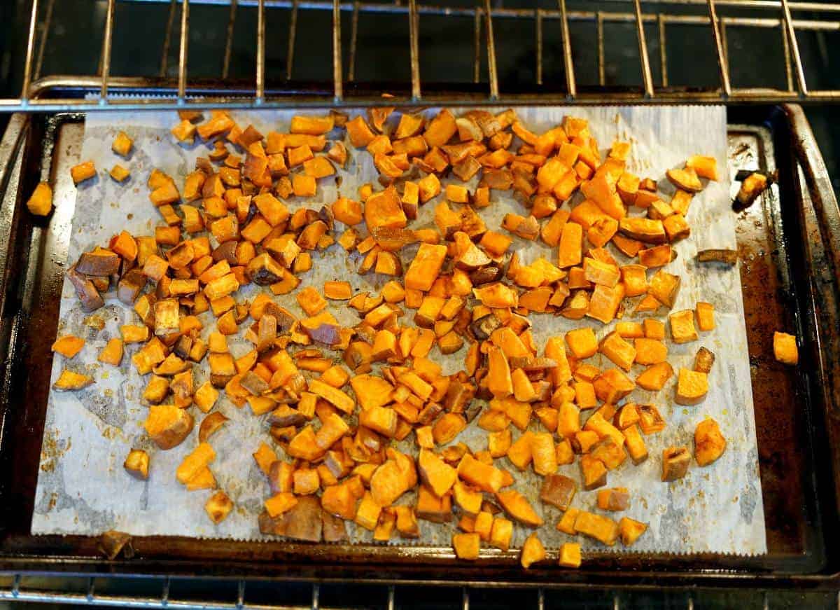 Diced sweet potatoes on a baking sheet roasting in the oven.