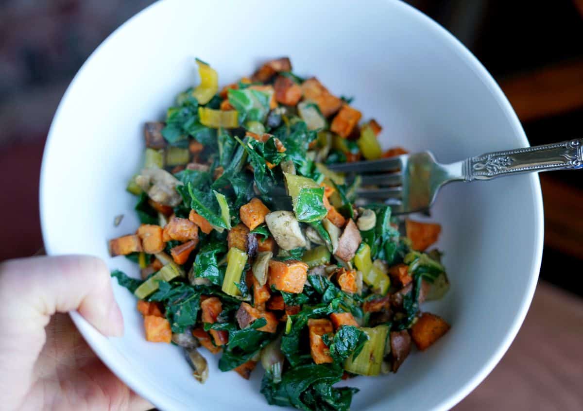 Rainbow chard, sweet potatoes, and mushrooms in a white bowl with a fork.