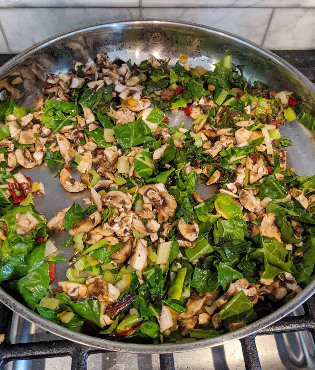 Rainbow chard and mushrooms in large pan on the stove.