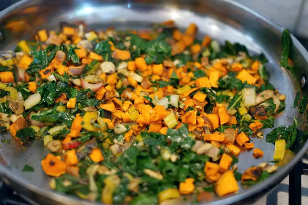 Rainbow chard, sweet potatoes, and mushrooms sauteeing in a pan on the stove.