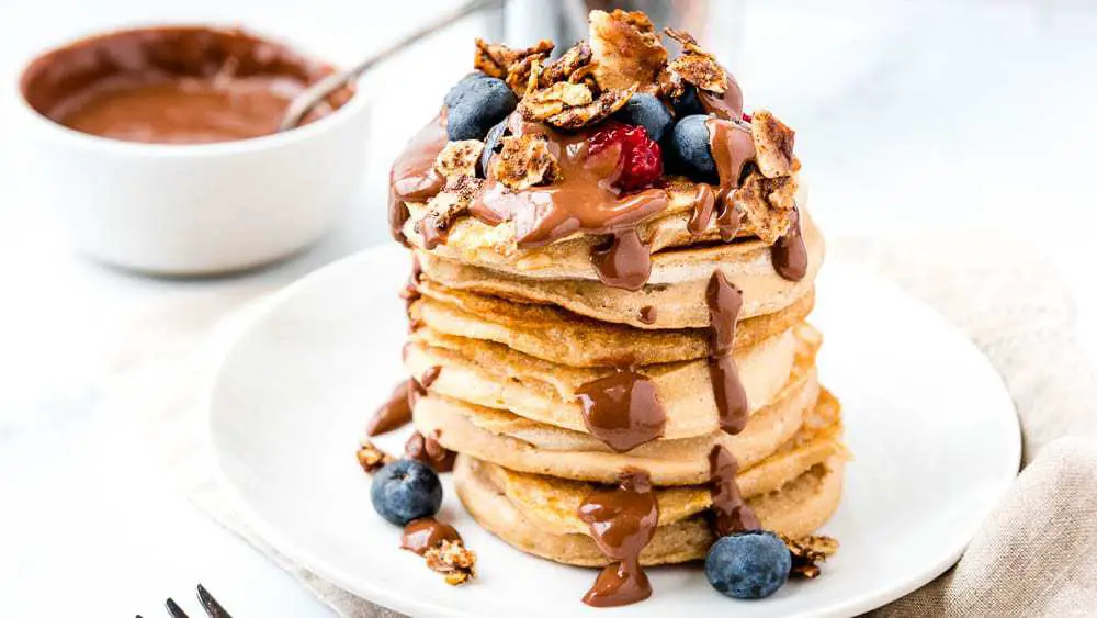 Stack of pancakes covered in berries, granola, and carob sauce.