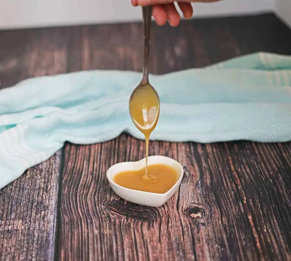 aip salted caramel sauce dripping from a spoon into a white heart shaped dish with a blue towel in the background