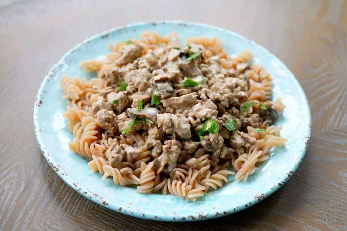 Ground turkey stroganoff over a bed of noddles on a blue plate sitting on a wooden table.