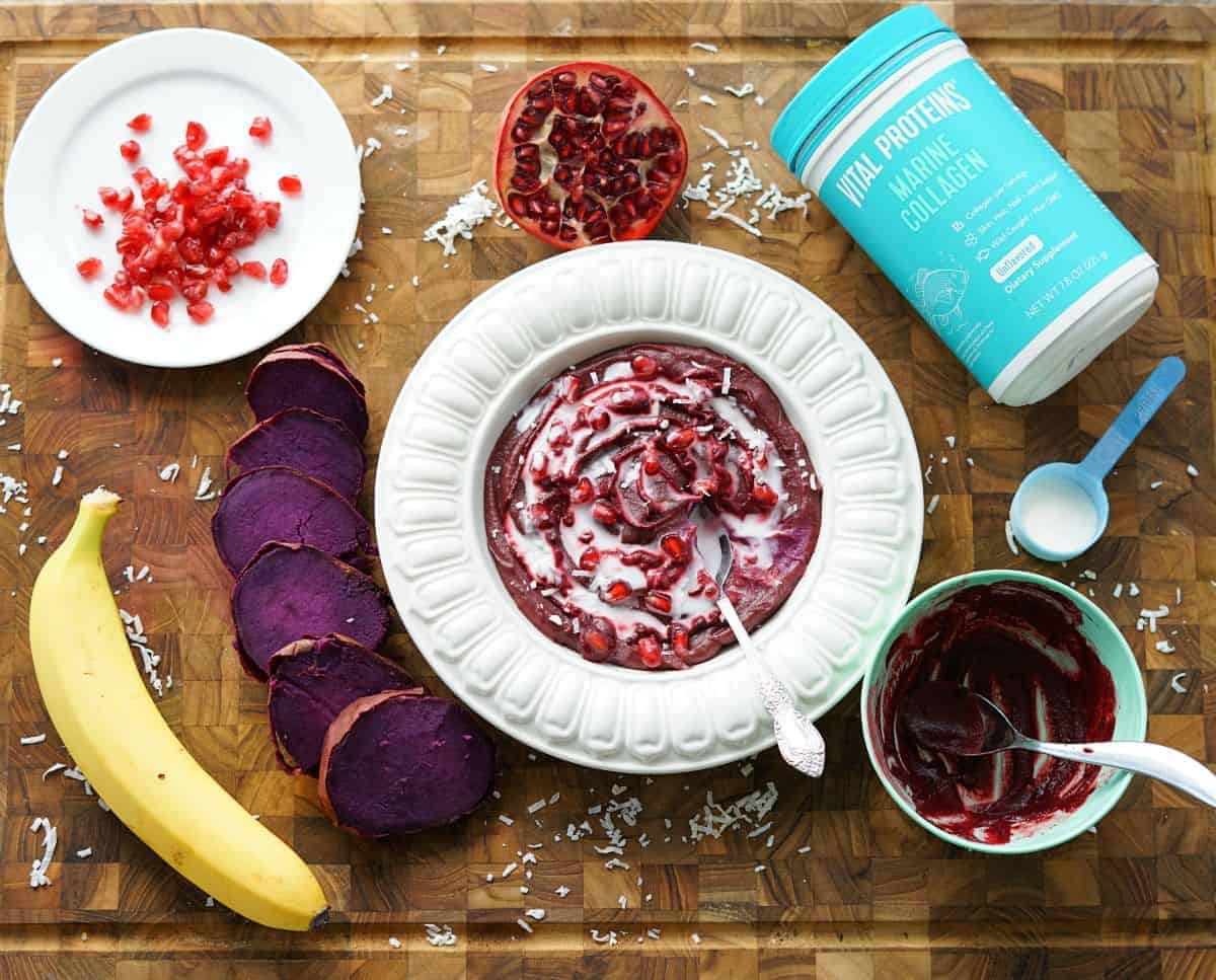 paleo purple sweet potato bowl surrounded by a banana, collagen powder, and pomegranate arils.