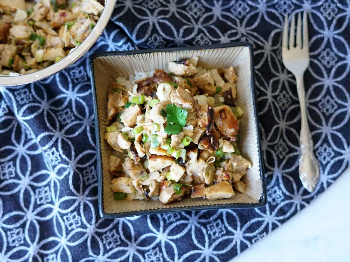 chicken kelaguen in a tan square bowl on a black and white towel with a fork next to it