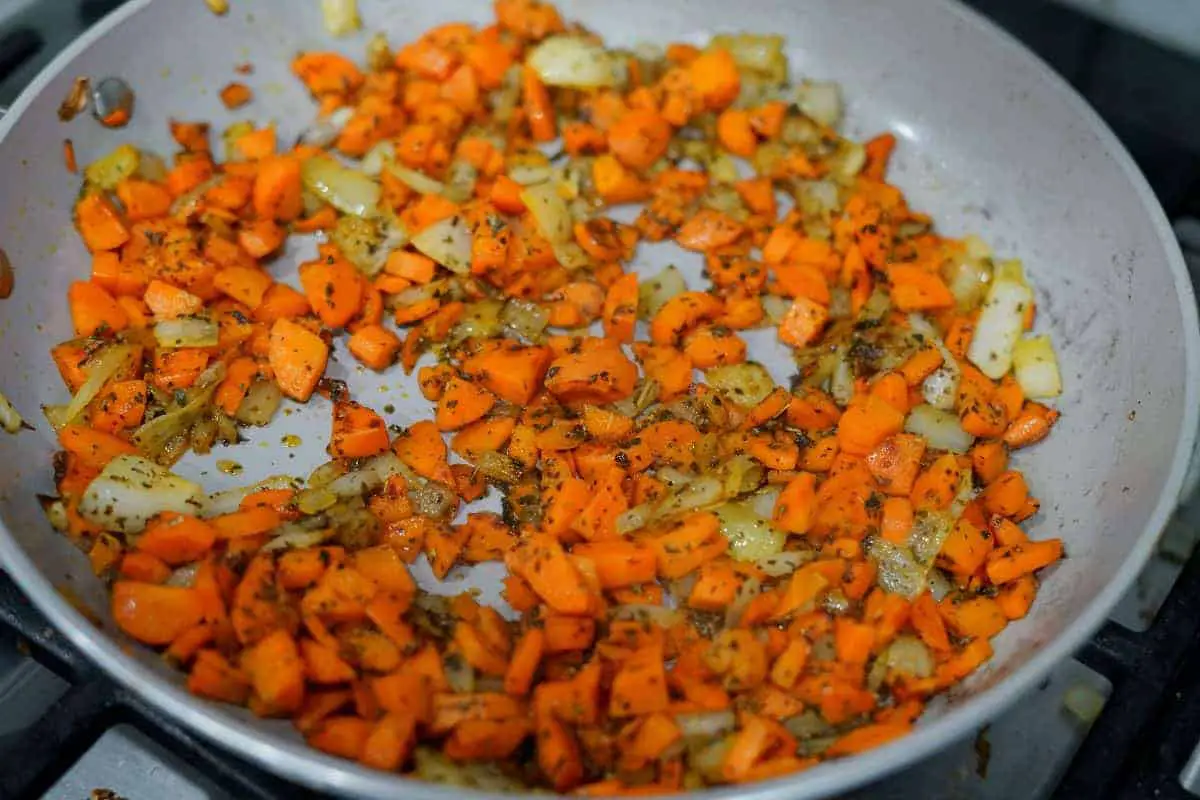 Carrots and onions sauteeing in a pan.