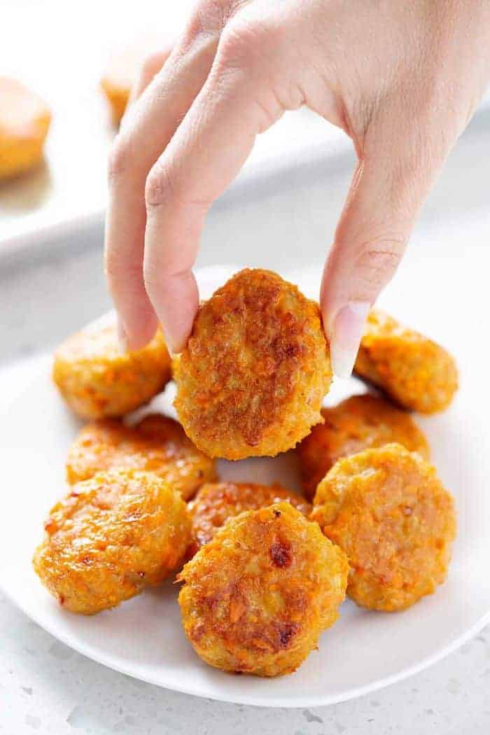 sweet potato poppers on a white plate with one being picked up by a hand