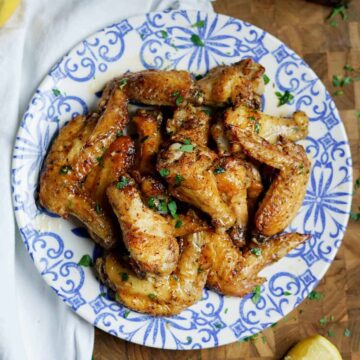 lemon pepper wings on a blue and white plate on top of a cutting board with a lemon nearby