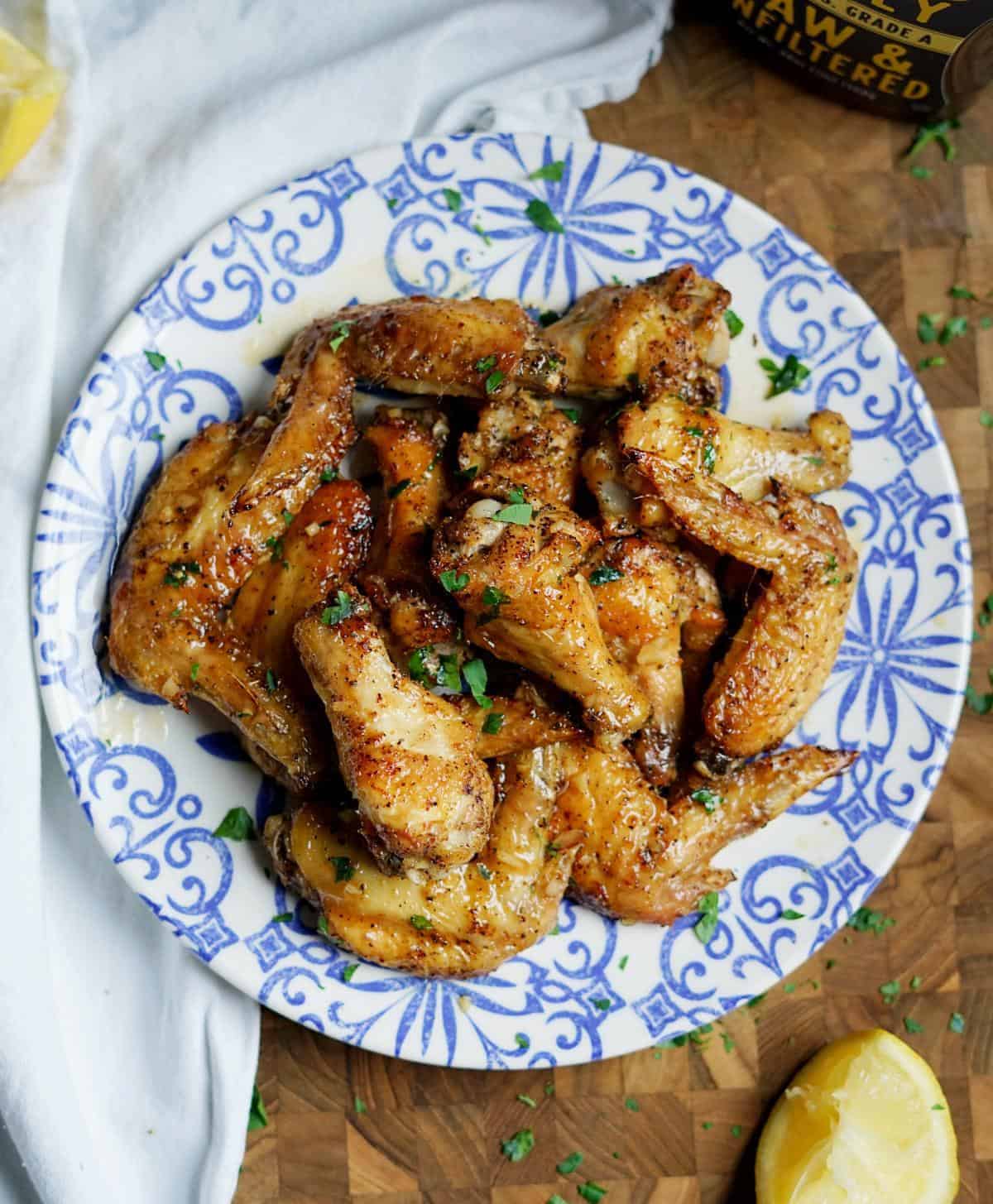 lemon pepper wings on a blue and white plate on top of a cutting board with a lemon nearby