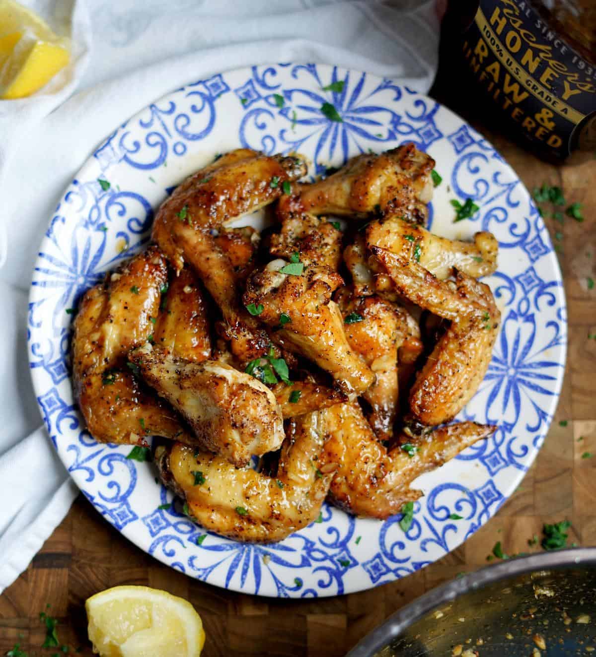 lemon pepper wings on a blue and white plate on top of a cutting board with a lemon and bottle of honey nearby