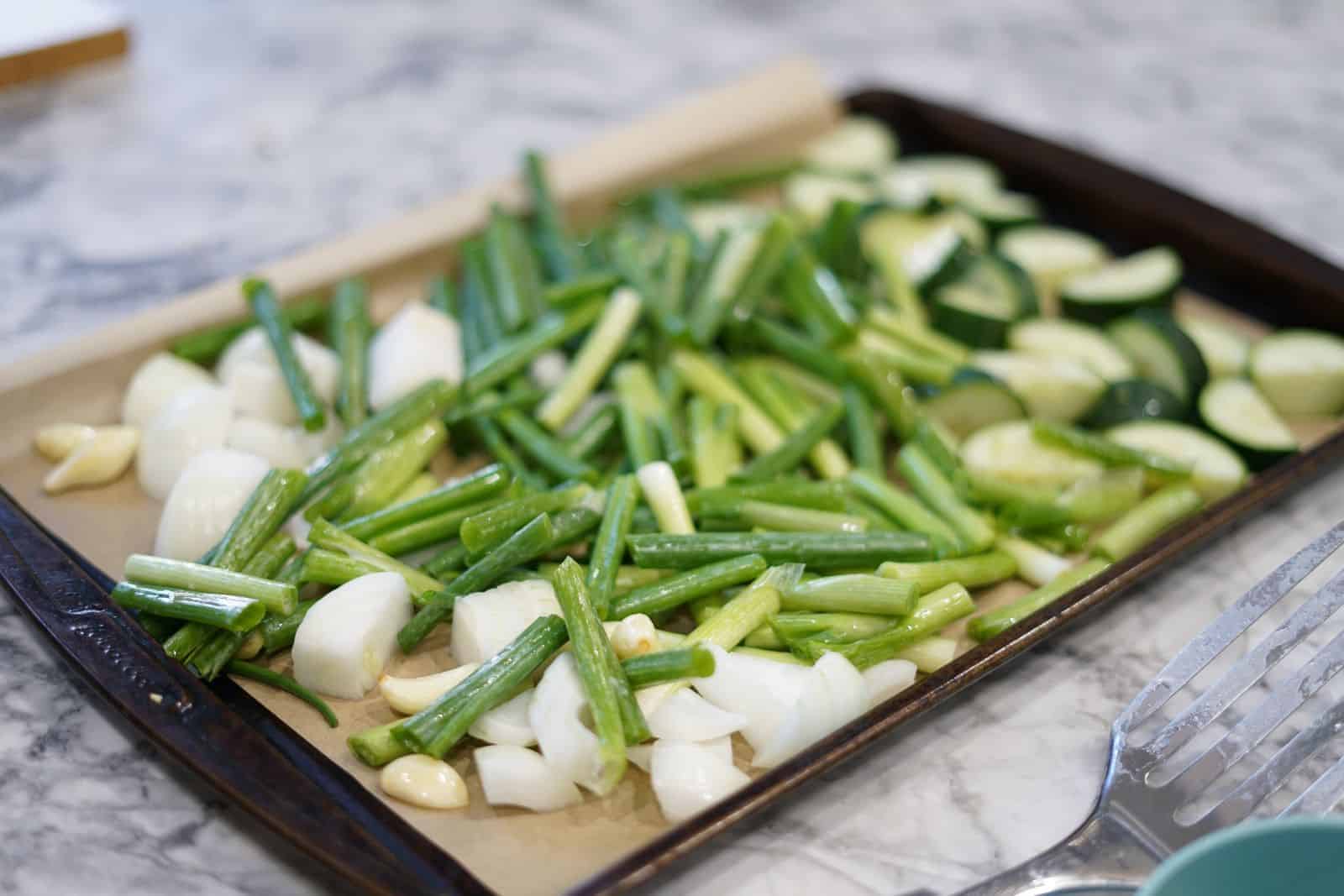 garlic, green onion, white onion, and cucumber on a baking sheet with parchment paper