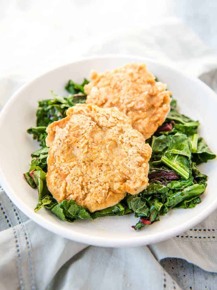 Two breaded chicken patties on a bed of greens on a white plate.