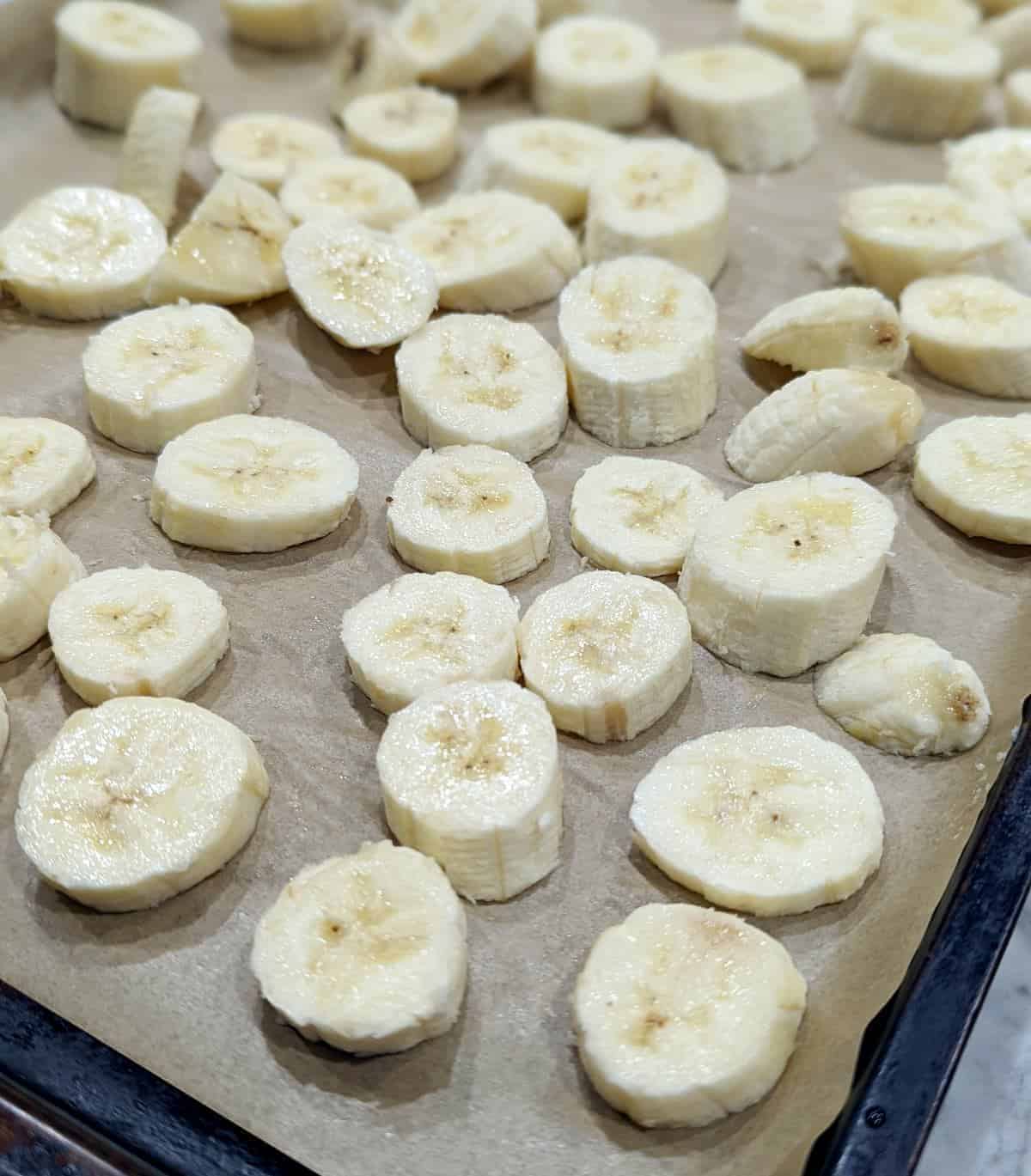 Sliced bananas on a parchment paper-lined baking sheet.