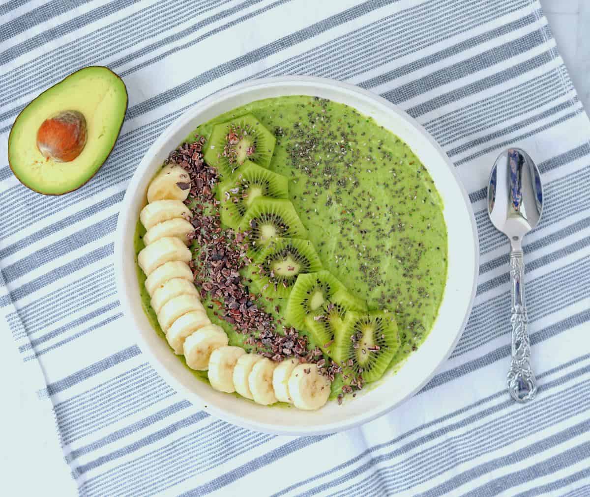 Overhead view of avocado banana kiwi smoothie bowl with sliced bananas, kiwis, cacao nibs, and chia seeds.