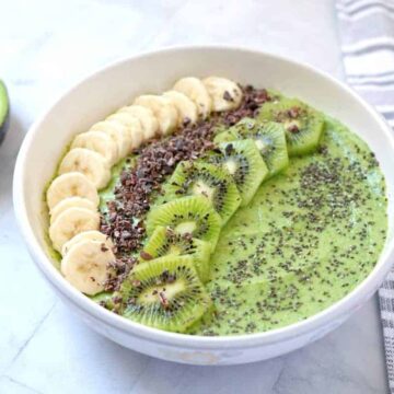 Close-up view of avocado banana kiwi smoothie bowl with sliced bananas, kiwis, cacao nibs, and chia seeds.