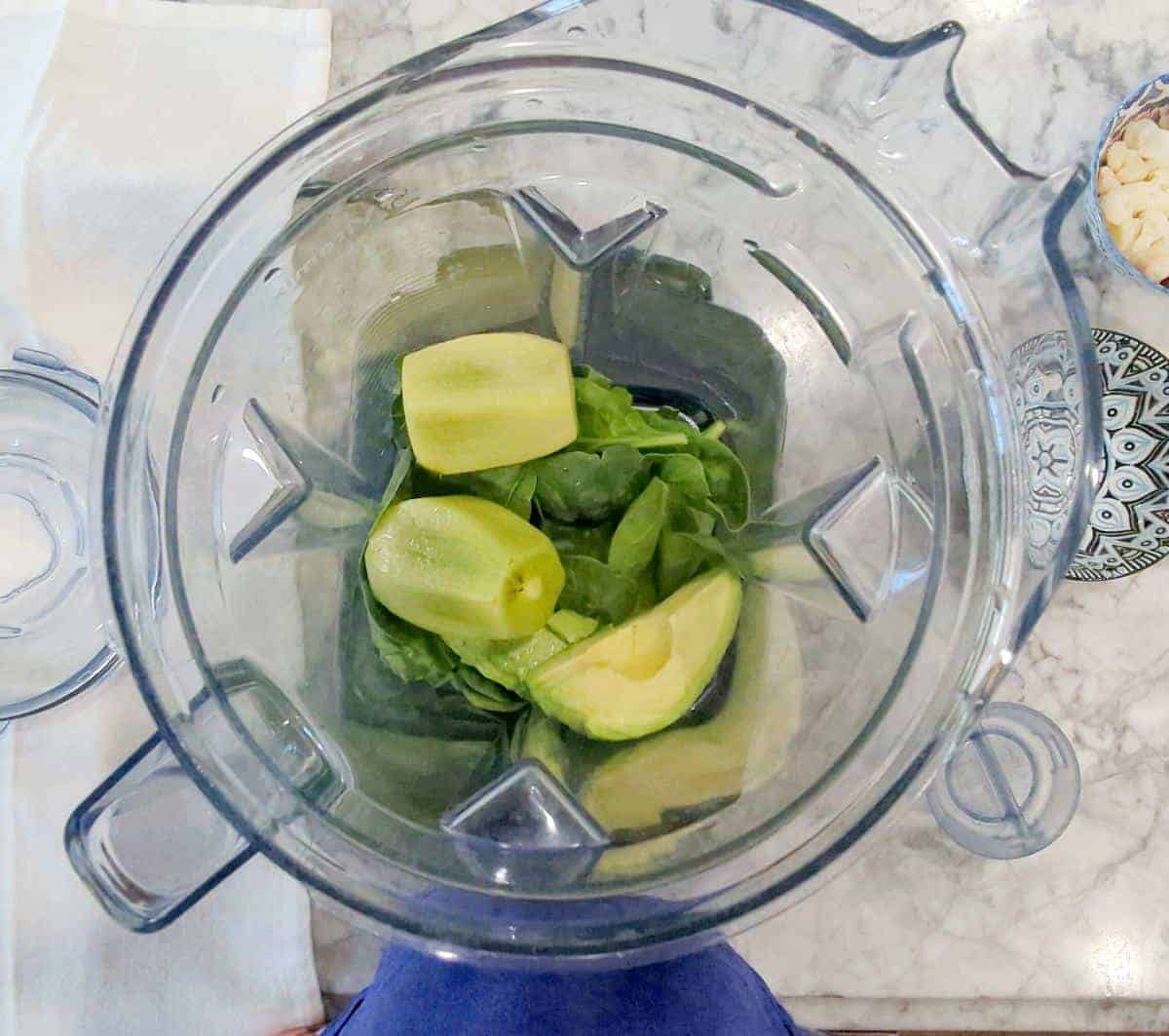 Overhead view of kiwis and spinach in the blender before blending.