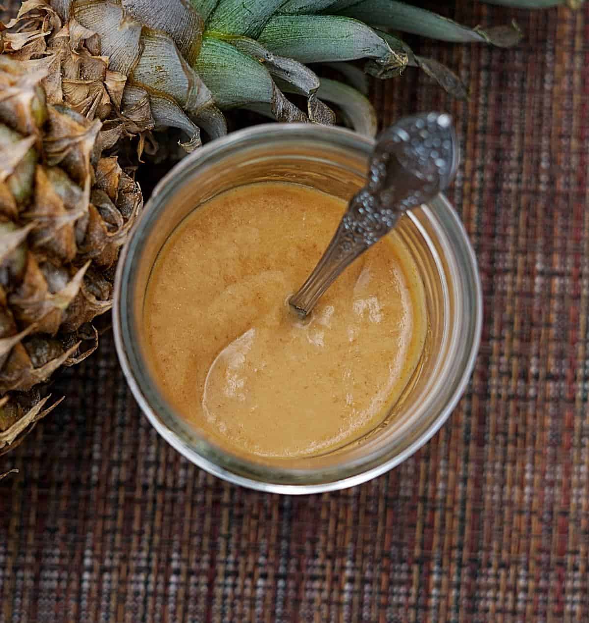 Overhead view of pineapple bacon sauce in a jar with a spoon next to a whole pineapple.
