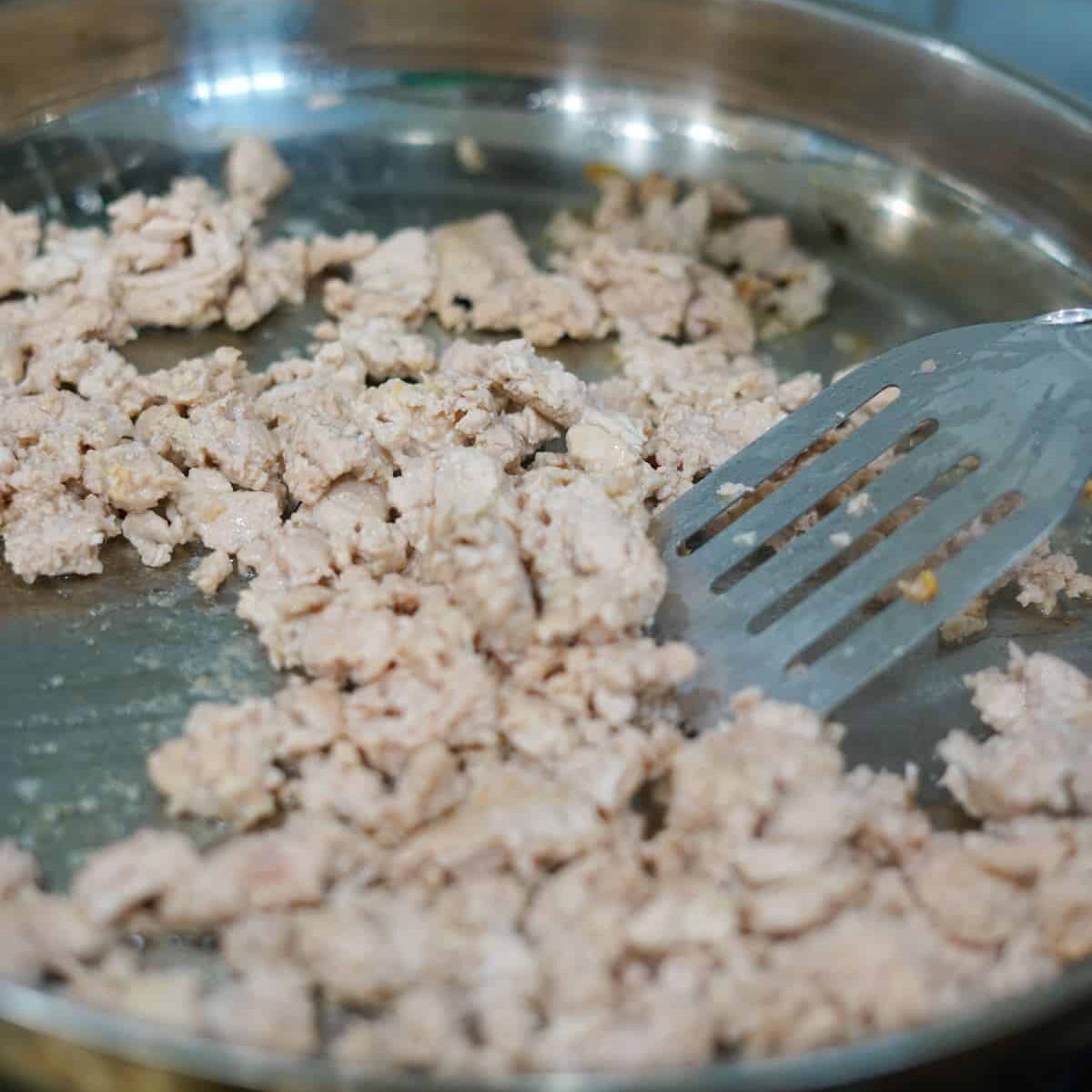Ground chicken in a metal pan with a spatula.