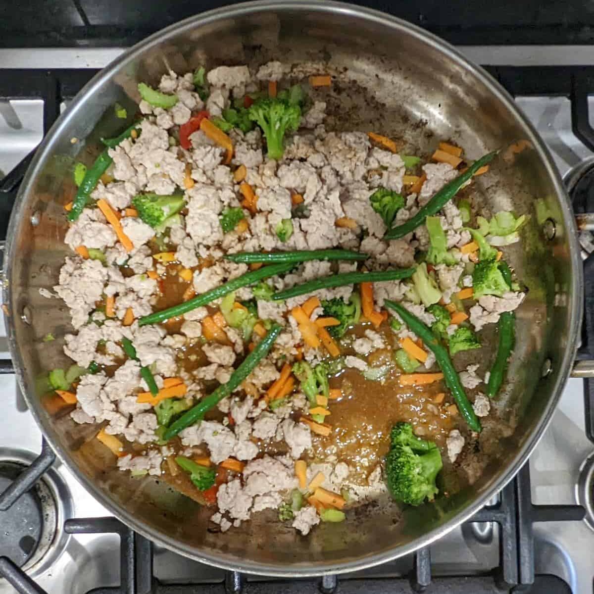 Stir fry sauce on top of ground chicken and vegetables in a pan.